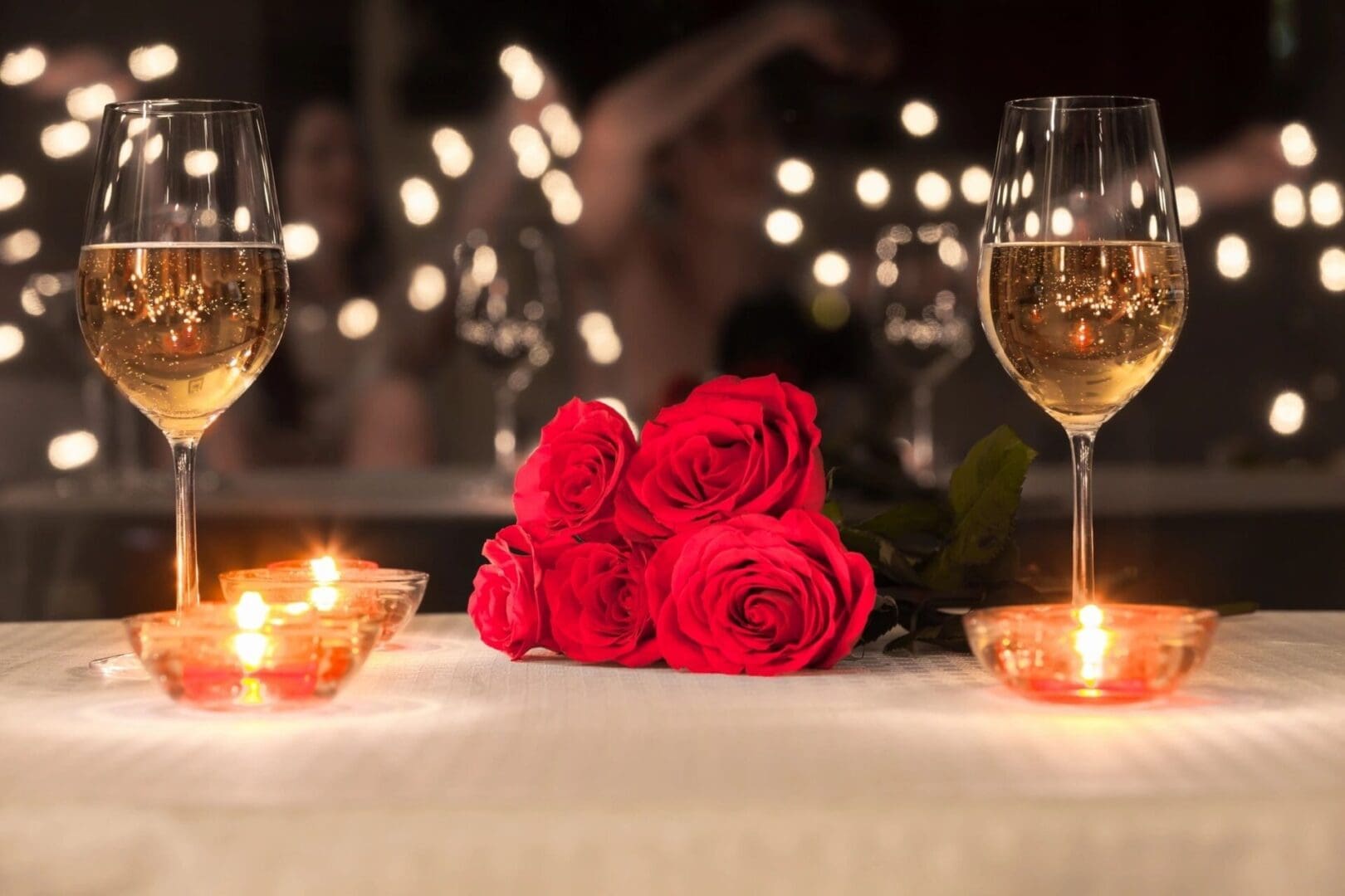 A table with three roses and two glasses of wine.