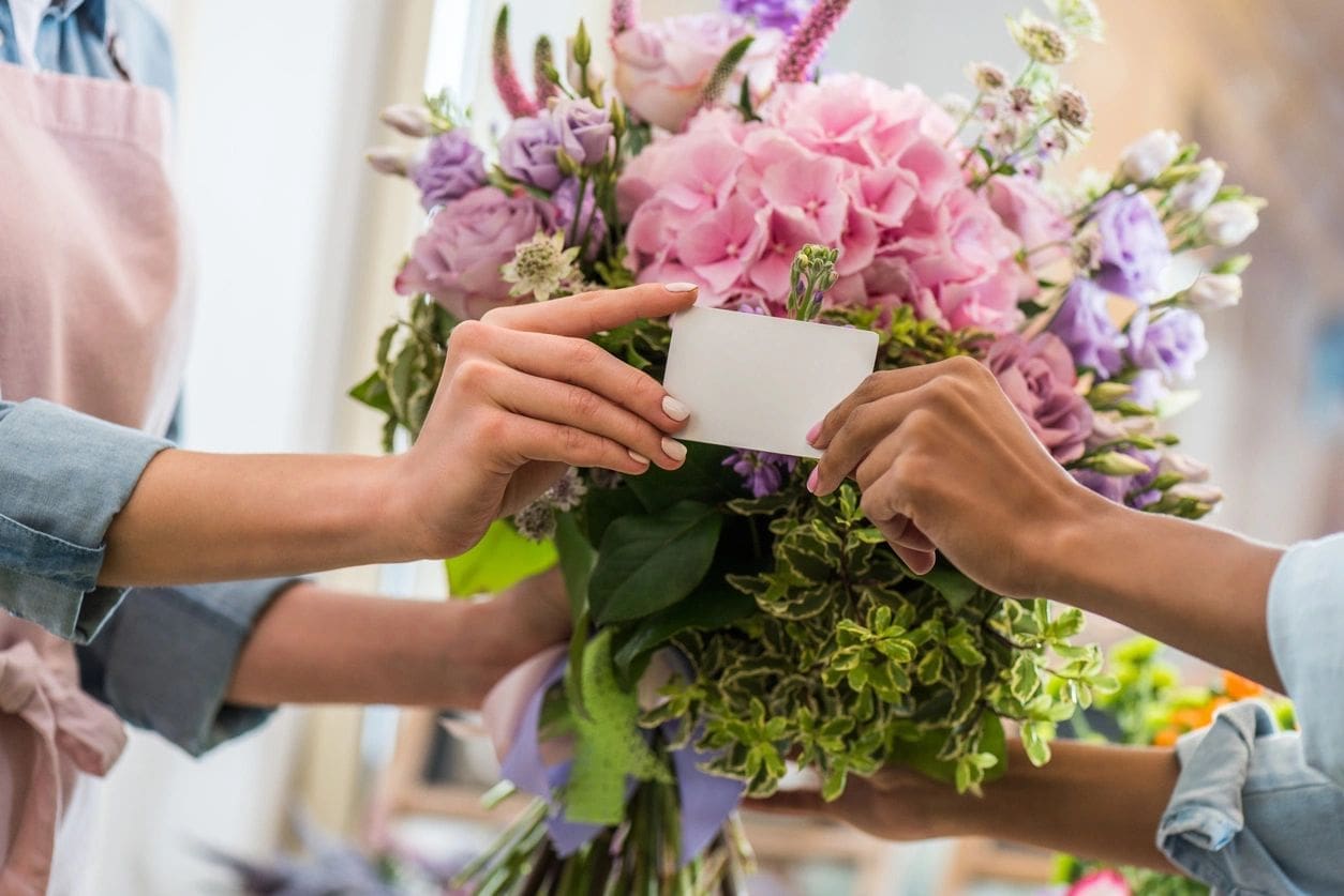 A person holding a card and flowers in a vase.