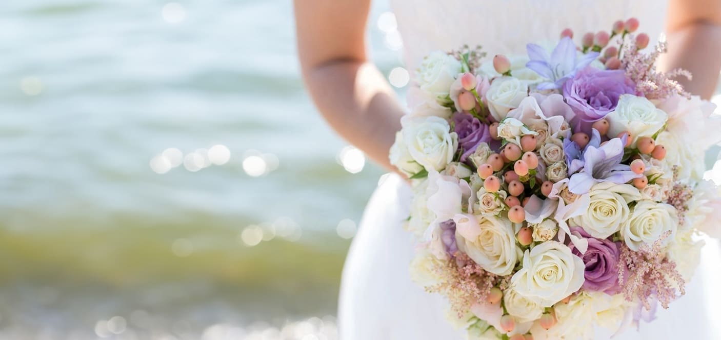 A bride holding her bouquet of flowers on the beach.